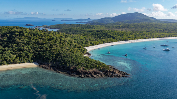 Aerial view of Whitehaven Beach with its iconic white sand and turquoise waters surrounded by lush green hills and boats anchored in the bay in Whitsundays Queensland Australia.