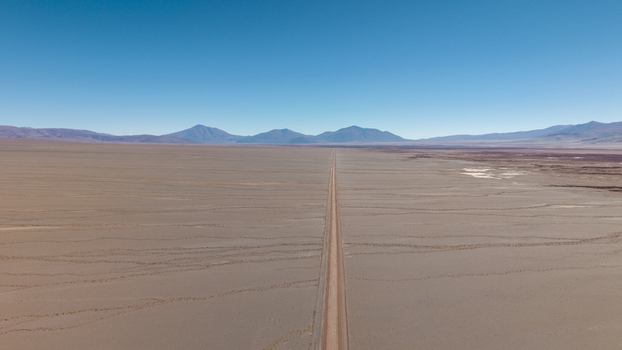 Aerial view of a long straight road stretching through the vast arid desert landscape towards distant mountains under a clear blue sky in Argentina. Aerial view of a long straight road stretching through the vast arid desert landscape towards distant mountains under a clear blue sky in Argentina.