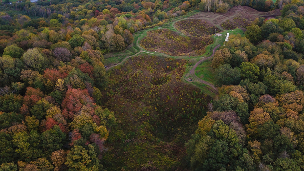 Aerial view of the World War 1 battlefield site of Vauquois Hill featuring craters trenches and a memorial monument surrounded by dense autumn forest in Vauquois Grand Est France.
