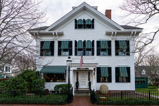 View of a historic white house with green striped awnings black shutters and an American flag on Martha s Vineyard in Edgartown Massachusetts United States.