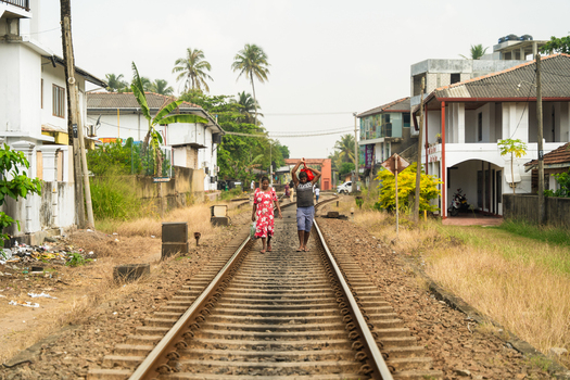 Sri Lanka 11 February 2026 View of two people walking along a railway track passing through a residential neighborhood with houses and palm trees.