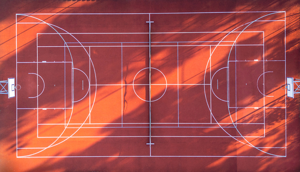 Aerial view of a red basketball court with white markings and long tree shadows cast across the surface in Suchacz Warmian Masurian Voiv Poland. Aerial view of a red basketball court with white markings and long tree shadows cast across the surface in Suchacz Warmian Masurian Voiv Poland.