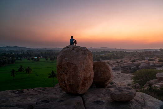 View of a person sitting on a large boulder overlooking the green landscape at sunset in Hampi Karnataka India. View of a person sitting on a large boulder overlooking the green landscape at sunset in Hampi Karnataka India.