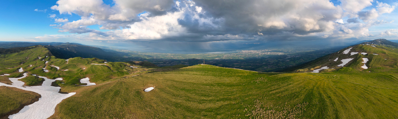 Aerial view of Le Colomby de Gex mountain ridge with patches of melting snow overlooking the Geneva basin under a dramatic cloudy sky Echenevex Auvergne Rhone Alpes France. Aerial view of Le Colomby de Gex mountain ridge with patches of melting snow overlooking the Geneva basin under a dramatic cloudy sky Echenevex Auvergne Rhone Alpes France.