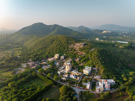 Aerial view of residential buildings nestled among lush green hills and trees in the outskirts of Udaipur Rajasthan India.