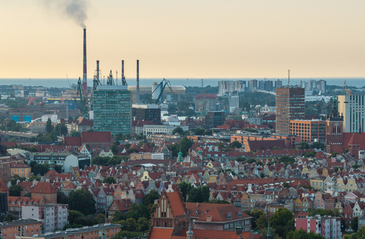 Aerial view of the historic city of Gdansk with dense red tiled rooftops industrial shipyard cranes and smoking chimneys in Gdansk Pomeranian Voivodeship Poland. Aerial view of the historic city of Gdansk with dense red tiled rooftops industrial shipyard cranes and smoking chimneys in Gdansk Pomeranian Voivodeship Poland.