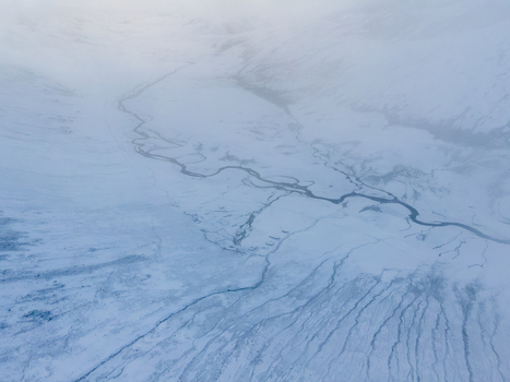 Aerial view of Babusar Pass with a winding river flowing through a vast snow covered mountain landscape under a misty sky Babusar KPK Pakistan.