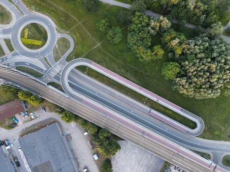 Aerial view of a modern pedestrian and bicycle bridge with a distinctive loop design surrounded by green spaces and a roundabout in Poland. Aerial view of a modern pedestrian and bicycle bridge with a distinctive loop design surrounded by green spaces and a roundabout in Poland.