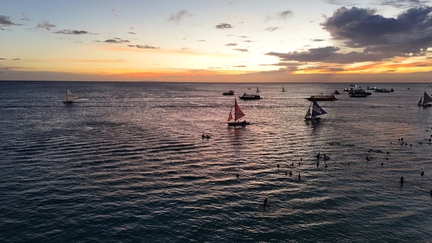 Malay Philippines 02 May 2026 Aerial view of Boracay Island featuring traditional sailboats on the calm sea and people swimming during a vibrant sunset.