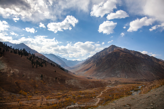 View of Astore Valley with autumn foliage dirt roads and rugged mountains under a blue sky in Astore Gilgit Pakistan. View of Astore Valley with autumn foliage dirt roads and rugged mountains under a blue sky in Astore Gilgit Pakistan.