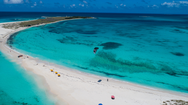 Aerial view of Los Roques archipelago with a kite surfer gliding over turquoise Caribbean waters white sand beaches and clear blue sky in Los Roques Dependencias Federales Venezuela. Aerial view of Los Roques archipelago with a kite surfer gliding over turquoise Caribbean waters white sand beaches and clear blue sky in Los Roques Dependencias Federales Venezuela.