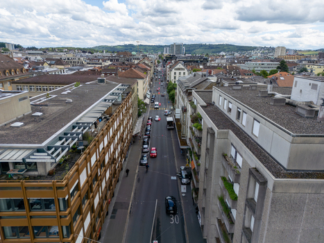 Aerial view of an urban street lined with modern and historic buildings parked cars and distant green hills under a cloudy sky in Biel Bienne Canton of Bern Switzerland. Aerial view of an urban street lined with modern and historic buildings parked cars and distant green hills under a cloudy sky in Biel Bienne Canton of Bern Switzerland.