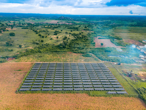 Aerial view of a large solar farm with rows of photovoltaic panels set in a rural landscape with green fields scattered trees and distant hills in Ogun State Nigeria.
