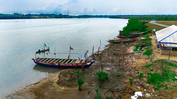 Aerial view of wooden boats moored along the muddy riverbank with a small building nearby in Minima Rivers Nigeria.