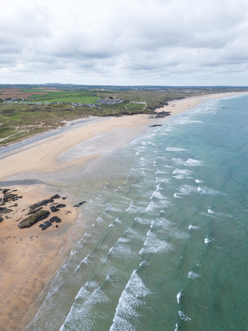 Aerial view of Godrevy Beach with turquoise waves rolling onto the sandy shore dark rocks and green coastal fields under a cloudy sky in Gwithian England United Kingdom. Aerial view of Godrevy Beach with turquoise waves rolling onto the sandy shore dark rocks and green coastal fields under a cloudy sky in Gwithian England United Kingdom.