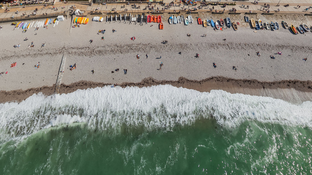 Aerial view of the rugged coastline where chalk cliffs meet the sea contrasting with the sandy beach dotted with sunbathers and colorful boats &Eacute;tretat Normandy France.