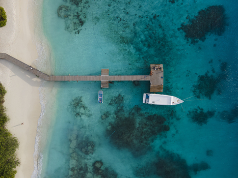 Aerial view of boat at end of pier and boardwalk on crystal clear blue ocean island Baa Atoll Maldives.