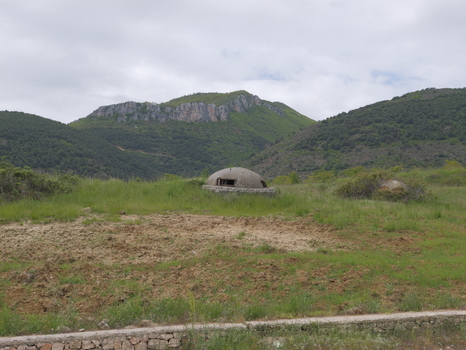 View of a historic concrete bunker situated in a grassy field with rolling mountains in the background in Pogradec Korce County Albania. View of a historic concrete bunker situated in a grassy field with rolling mountains in the background in Pogradec Korce County Albania.