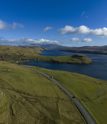 Aerial view of the winding coastal road near Gesto Bay Viewpoint overlooking the blue waters and distant mountains in Isle of Skye Scotland United Kingdom.