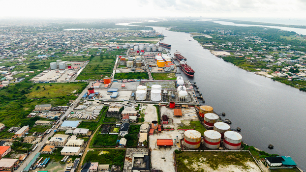Aerial view of the industrial port area in Satellite Town with large storage tanks cargo ships docked along the river and surrounding urban development in Lagos Lagos Nigeria.