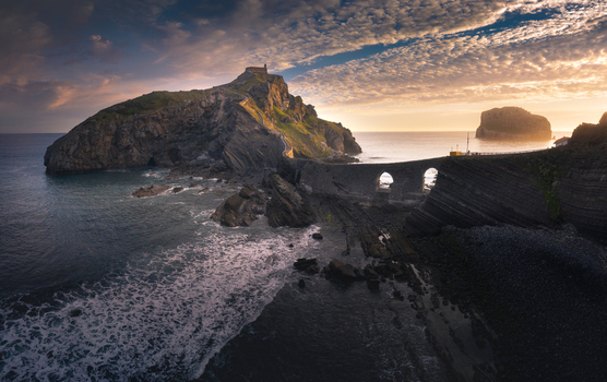 Aerial view of Gaztelugatxe island with its iconic winding stone bridge and rugged cliffs under a warm sunset sky Gaztelugatxeko Doniene Basque Country Spain. Aerial view of Gaztelugatxe island with its iconic winding stone bridge and rugged cliffs under a warm sunset sky Gaztelugatxeko Doniene Basque Country Spain.