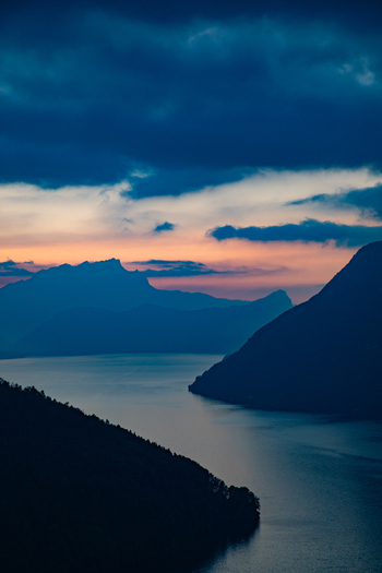 Aerial view of the Swiss Alps at sunset with dramatic mountain silhouettes a calm lake reflecting the twilight sky and deep blue shadows in Airolo Ticino Switzerland. Aerial view of the Swiss Alps at sunset with dramatic mountain silhouettes a calm lake reflecting the twilight sky and deep blue shadows in Airolo Ticino Switzerland.