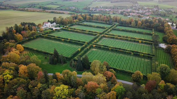 Aerial view of the World War 1 Meuse Argonne American Cemetery and Memorial with rows of white grave markers in manicured lawns and autumn trees in Romagne sous Montfaucon Grand Est France.