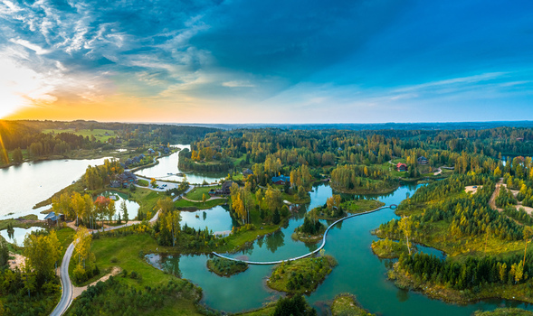Aerial view of a serene lake system surrounded by lush autumn forests winding wooden walkways and small cabins under a vibrant sunset sky in Latvia. Aerial view of a serene lake system surrounded by lush autumn forests winding wooden walkways and small cabins under a vibrant sunset sky in Latvia.