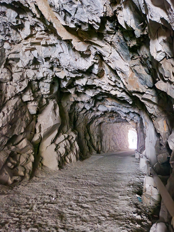 View of the rugged unpaved rock tunnel leading to the remote village of Malana featuring natural stone walls and bright daylight at the exit in Malana Himachal Pradesh India.