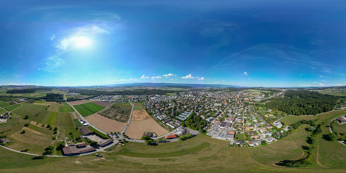 Aerial view of the town of Lyss featuring residential areas industrial zones and vast agricultural fields under a bright sun and blue sky Lyss Canton of Bern Switzerland.