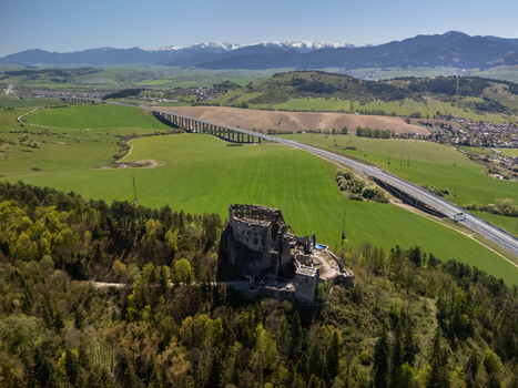 Aerial view of Castle Likava ruins on a forested hill with a highway viaduct and snow capped mountains in the background in Likavka Zilina Region Slovakia. Aerial view of Castle Likava ruins on a forested hill with a highway viaduct and snow capped mountains in the background in Likavka Zilina Region Slovakia.