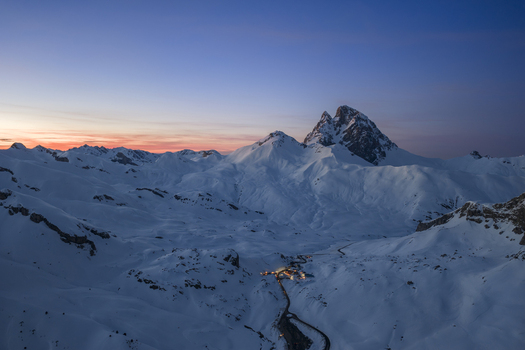 Aerial view of Pyrenees mountains covered in snow with a winding road and illuminated buildings in the valley at dusk Spain. Aerial view of Pyrenees mountains covered in snow with a winding road and illuminated buildings in the valley at dusk Spain.