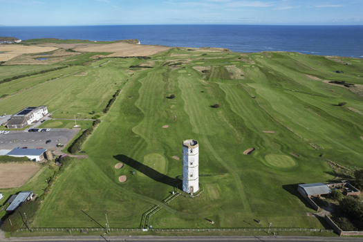 Aerial view of the historic Old Flamborough Lighthouse standing on a lush green golf course with sand bunkers and the blue sea in the background in Bridlington England United Kingdom. Aerial view of the historic Old Flamborough Lighthouse standing on a lush green golf course with sand bunkers and the blue sea in the background in Bridlington England United Kingdom.