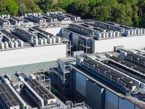 Aerial view of a large data center featuring rows of cooling units on the roof industrial infrastructure and surrounding trees in the United Kingdom.