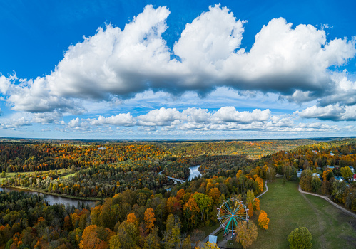 Aerial view of the Sigulda landscape in autumn with a ferris wheel the Gauja river winding through forests and blue sky with clouds in Sigulda Sigulda Municipality Latvia. Aerial view of the Sigulda landscape in autumn with a ferris wheel the Gauja river winding through forests and blue sky with clouds in Sigulda Sigulda Municipality Latvia.
