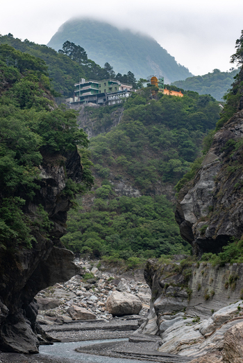 View of Taroko National Park featuring a rocky gorge with a riverbed lush green forested slopes and a building complex perched on the hillside in Xiulin Township Hualien County Taiwan.