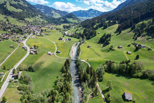 Aerial view of the picturesque village of Rougemont with the Sarine river flowing through lush green meadows and alpine forests Rougemont Vaud Switzerland. Aerial view of the picturesque village of Rougemont with the Sarine river flowing through lush green meadows and alpine forests Rougemont Vaud Switzerland.