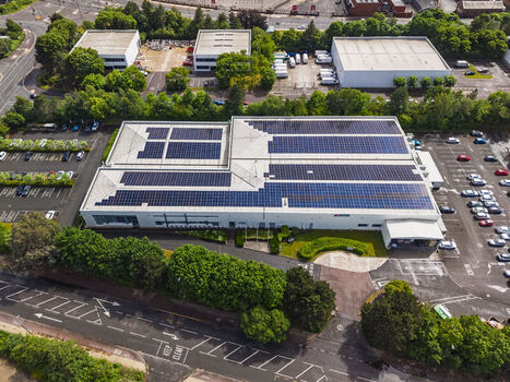 Aerial view of a commercial building with extensive rooftop solar panels surrounded by a parking lot green trees and nearby roads in Stretford England United Kingdom.