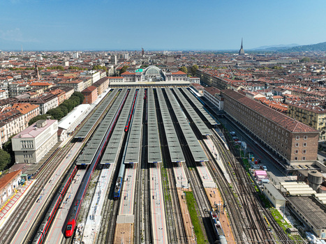 Aerial view of Porta Nuova railway station with multiple platforms red high speed trains and the city skyline under a clear blue sky Turin Piedmont Italy. Aerial view of Porta Nuova railway station with multiple platforms red high speed trains and the city skyline under a clear blue sky Turin Piedmont Italy.