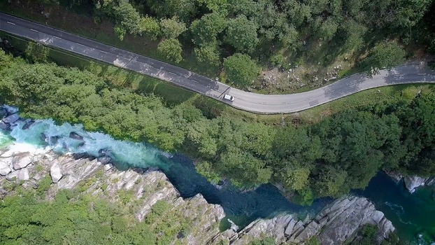 Aerial view of the winding road and turquoise waters of Valle Verzasca surrounded by lush green forest and rocky banks in Verzasca Ticino Switzerland. Aerial view of the winding road and turquoise waters of Valle Verzasca surrounded by lush green forest and rocky banks in Verzasca Ticino Switzerland.