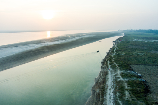 Aerial view of the Padma River at sunset with a small boat navigating the calm waters sandy riverbanks and lush green fields along the shore in Rajshahi Rajshahi Division Bangladesh.