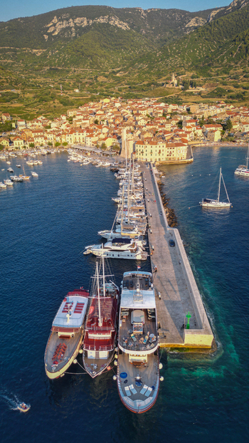 Aerial view of the harbor and historic town of Komiza with boats docked at the pier and lush green mountains in the background Komiza Split Dalmatia County Croatia.