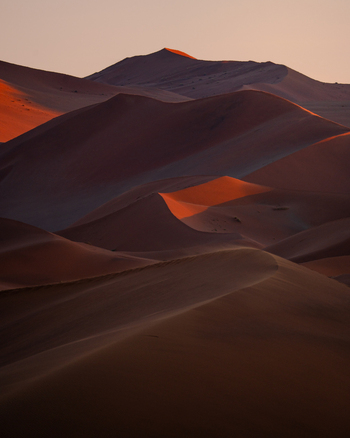 View of the warm glow of the setting sun painting the rippled sand dunes in shades of orange and brown creating a stunning desert landscape Sossusvlei Namibia. View of the warm glow of the setting sun painting the rippled sand dunes in shades of orange and brown creating a stunning desert landscape Sossusvlei Namibia.