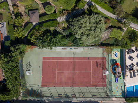 Aerial view of a tennis court with a red surface and green perimeter surrounded by lush trees and a small playground area in Istanbul Istanbul Turkey. Aerial view of a tennis court with a red surface and green perimeter surrounded by lush trees and a small playground area in Istanbul Istanbul Turkey.