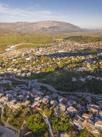 Aerial view of the historic town of Gjirokaster featuring traditional stone houses winding roads and the surrounding mountainous landscape in Gjirokaster Gjirokaster County Albania. Aerial view of the historic town of Gjirokaster featuring traditional stone houses winding roads and the surrounding mountainous landscape in Gjirokaster Gjirokaster County Albania.