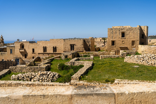 View of ancient limestone buildings and stone ruins with green grass under a clear blue sky in Zebbug Gozo Region Malta. View of ancient limestone buildings and stone ruins with green grass under a clear blue sky in Zebbug Gozo Region Malta.