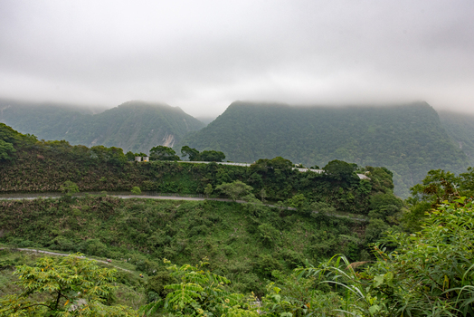 View of the winding road through the lush green mountains of Taroko National Park under a cloudy sky in Xiulin Township Hualien County Taiwan.