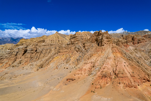 Aerial view of the arid rocky mountain landscape with dramatic rock formations and desert terrain under a clear blue sky in Nepal.