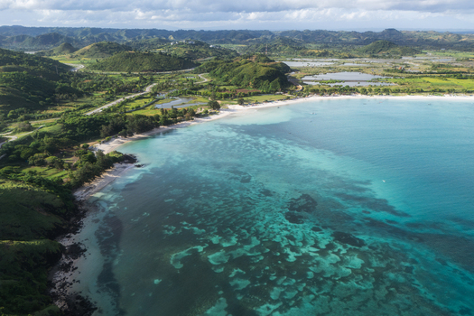 Aerial view of Tanjung Aan Beach featuring white sand turquoise waters and lush green hills in Kecamatan Pujut Nusa Tenggara Barat Indonesia.
