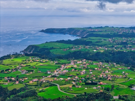 Aerial view of Silence Beach Viewpoint with lush green meadows scattered houses and rugged cliffs along the Cantabrian Sea in Cudillero Asturias Spain.